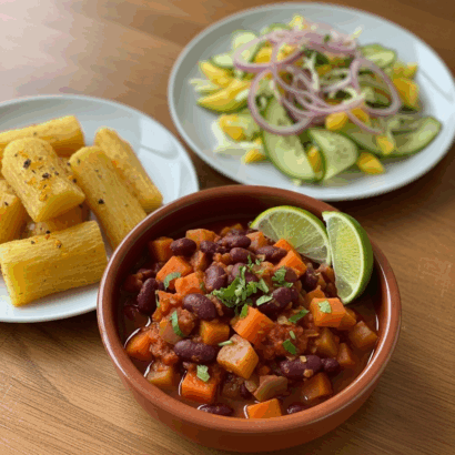 A bowl of Nicaraguan-style red bean stew with carrot and potato cubes garnished with cilantro and lime wedges, served alongside golden fried yuca sticks and a cucumber–green mango–red onion slaw on white plates.