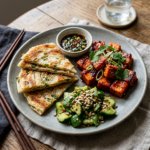 A plated meal with sliced scallion pancakes, glazed tofu topped with spring onion and herbs, a cucumber salad sprinkled with sunflower seeds, and a small bowl of dipping sauce on a rustic wooden table.